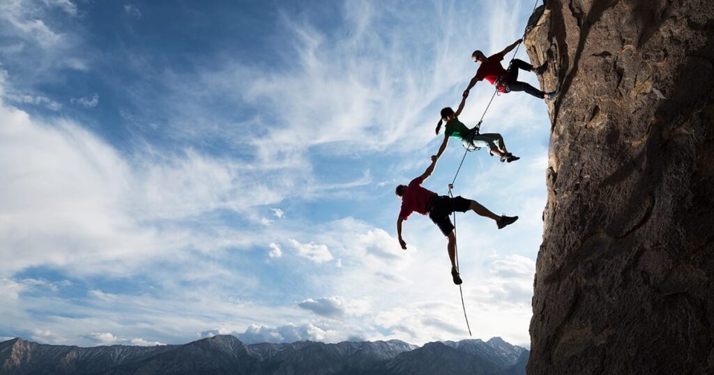 three climbers holding hands while scaling a mountain