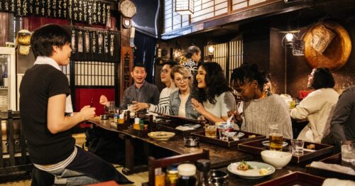 Group of friends ordering food in Japanese Izakaya. Waiter taking food order from happy group of friends, night out, drinking, eating