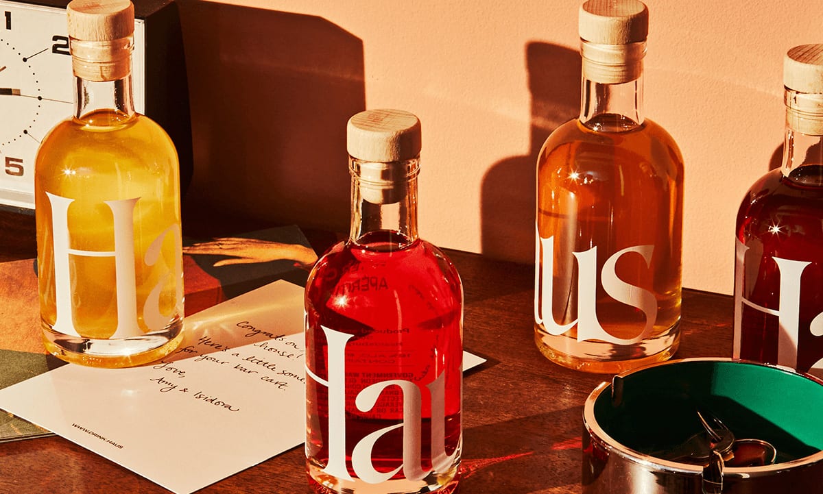 four bottles of haus brand sprits arranged on a tabletop next to a clock and an ashtray